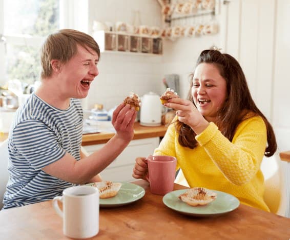 Two friends laughing together over cupcakes and tea in a kitchen