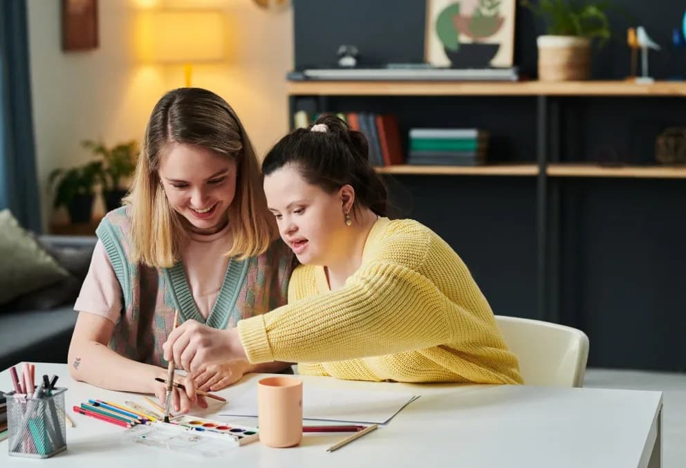 A support worker and a young woman painting together at a table at home