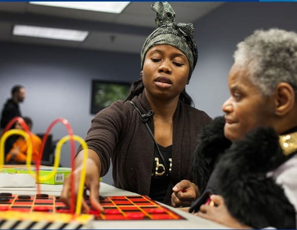 A support worker helping someone with a hands-on activity at a table